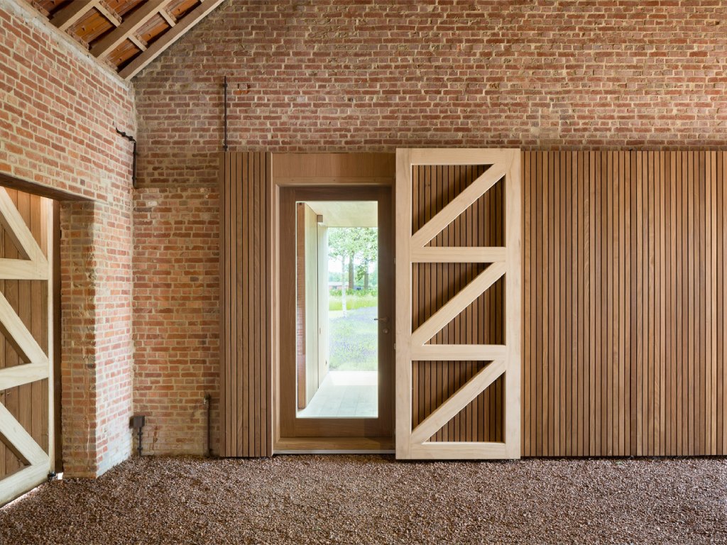 Modern barn door with light wood finish sliding open to reveal a brick patio.