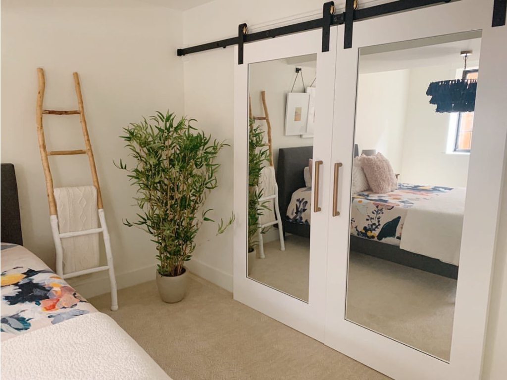 A bedroom with a sliding barn door with mirrors, a ladder leaning against the wall, and a potted plant.