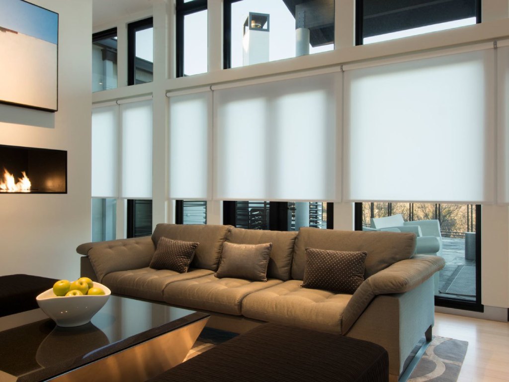 Modern living room with white roller shades covering large windows.