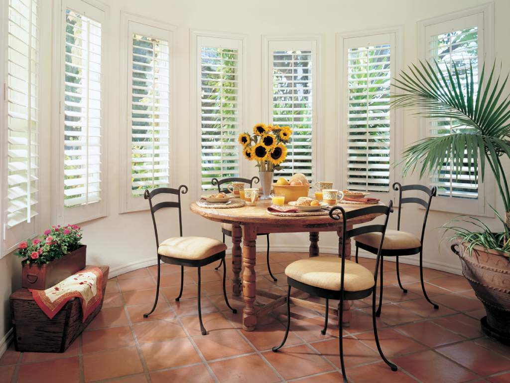 Bright dining room with white plantation shutters covering bay windows.